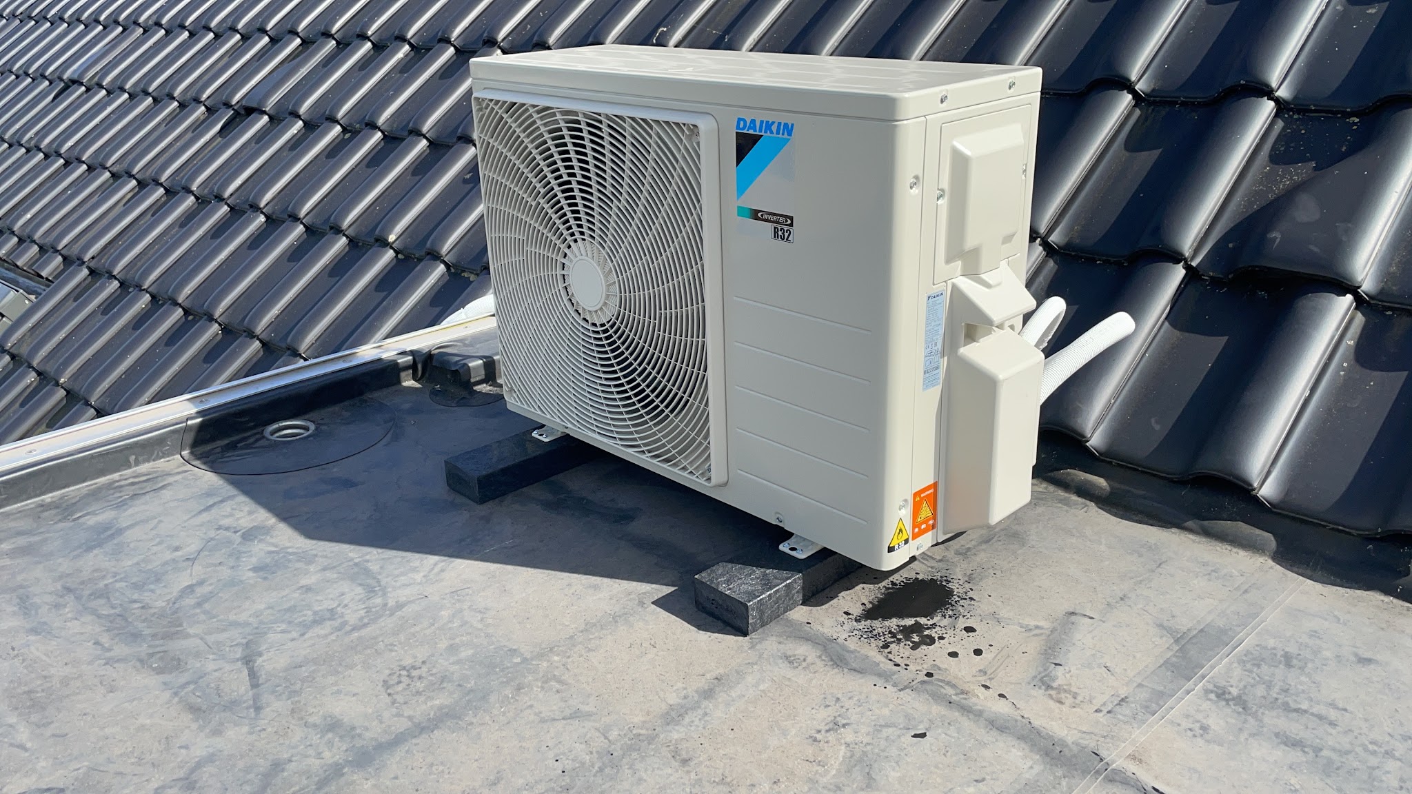 Daikin buitenunit op een plat dak naast een pannendak