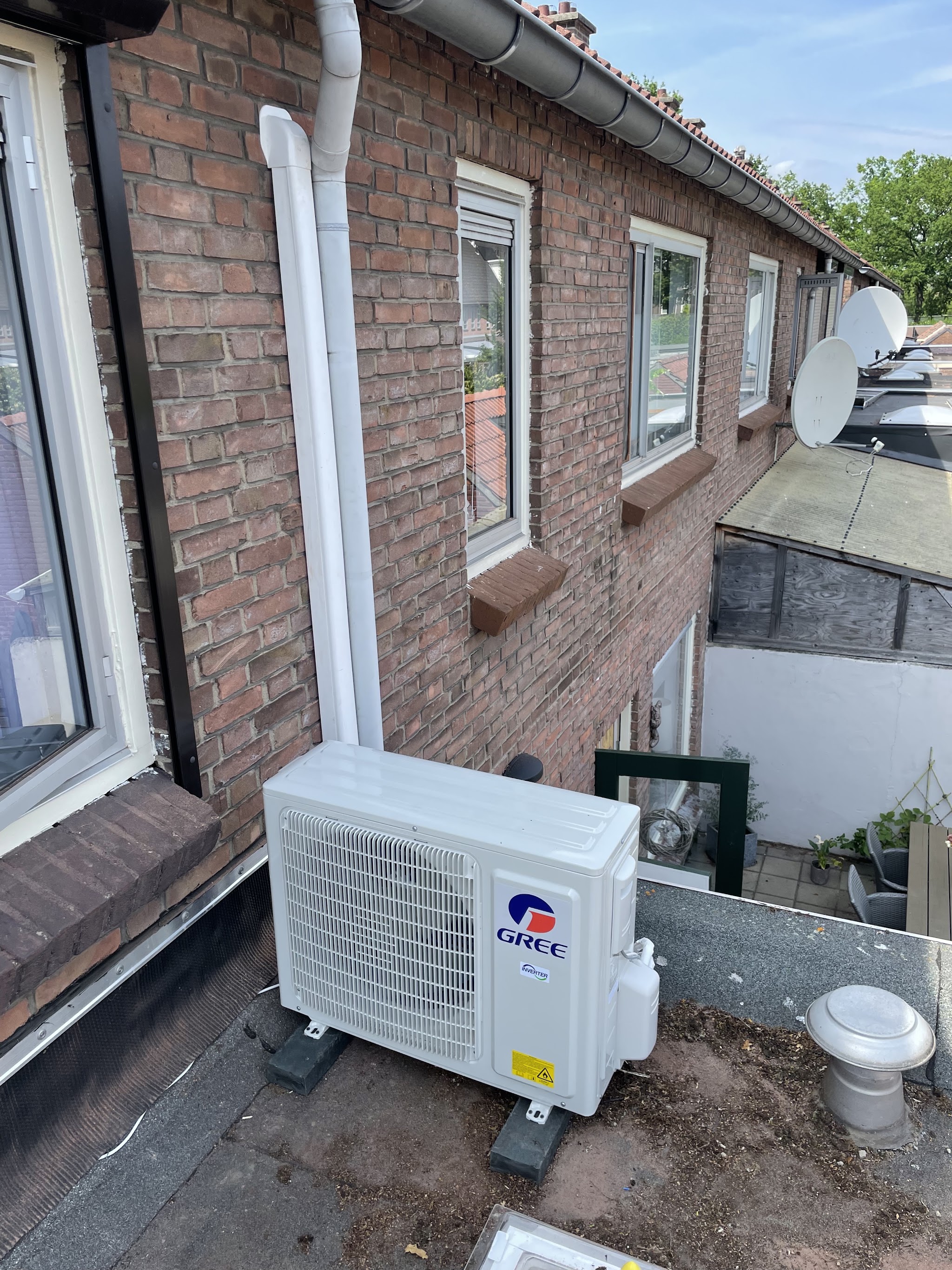 Gree buitenunit op een plat dak bij een rijtjeswoning
