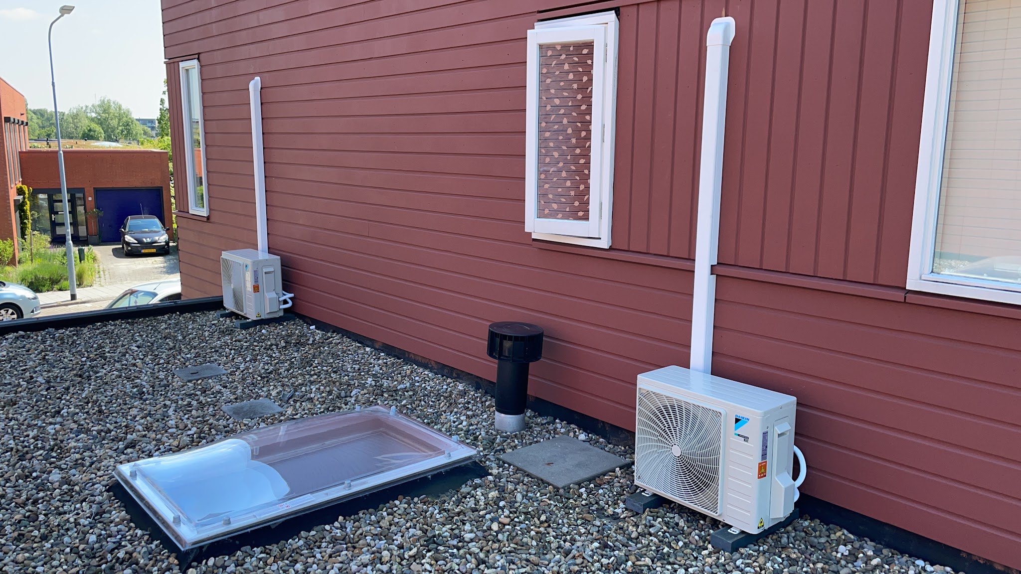 Twee Daikin buitenunits op een grinddak langs een rode houten gevel