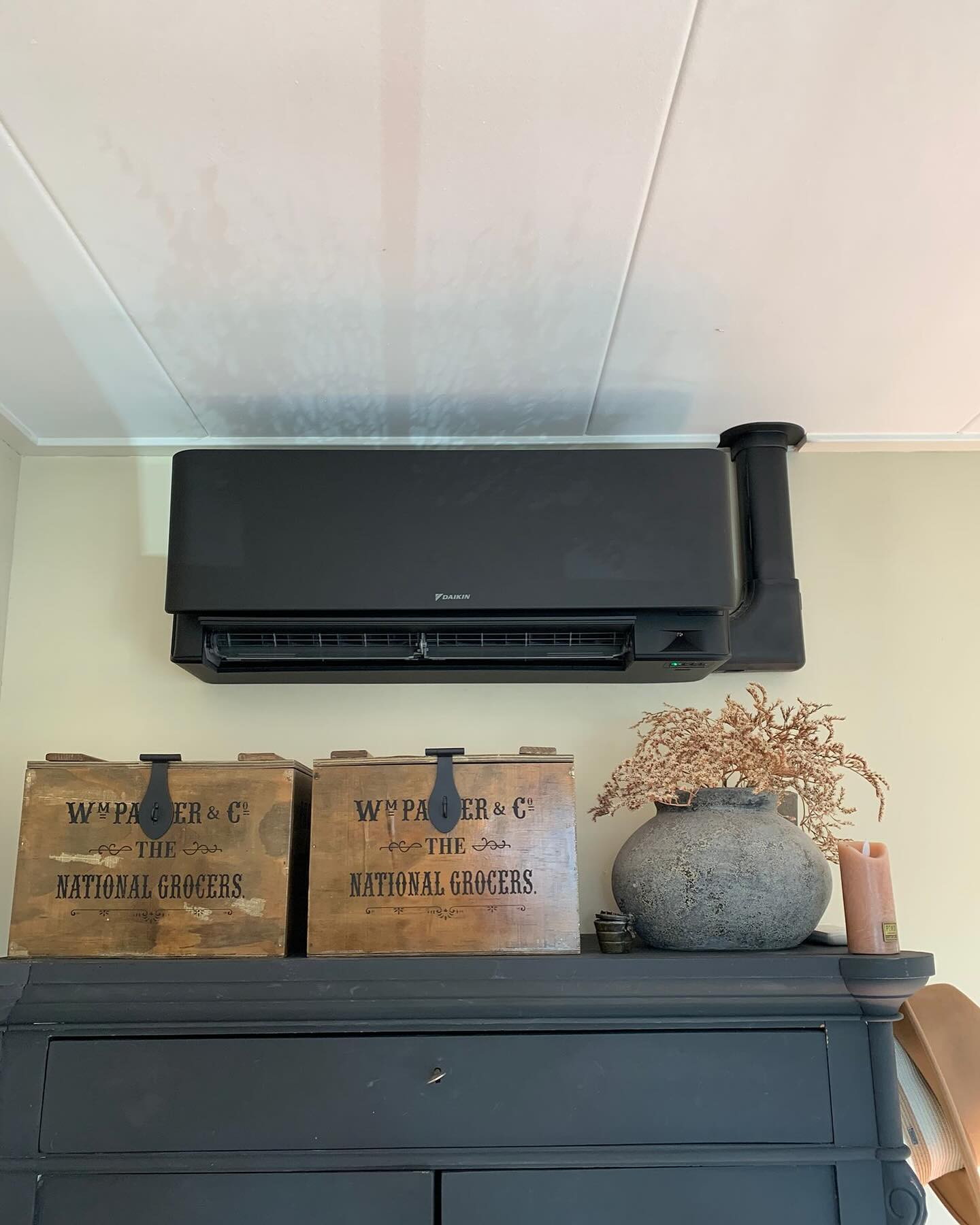 Zwarte Daikin binnenunit met zwarte leidingkoker boven een donkere kast