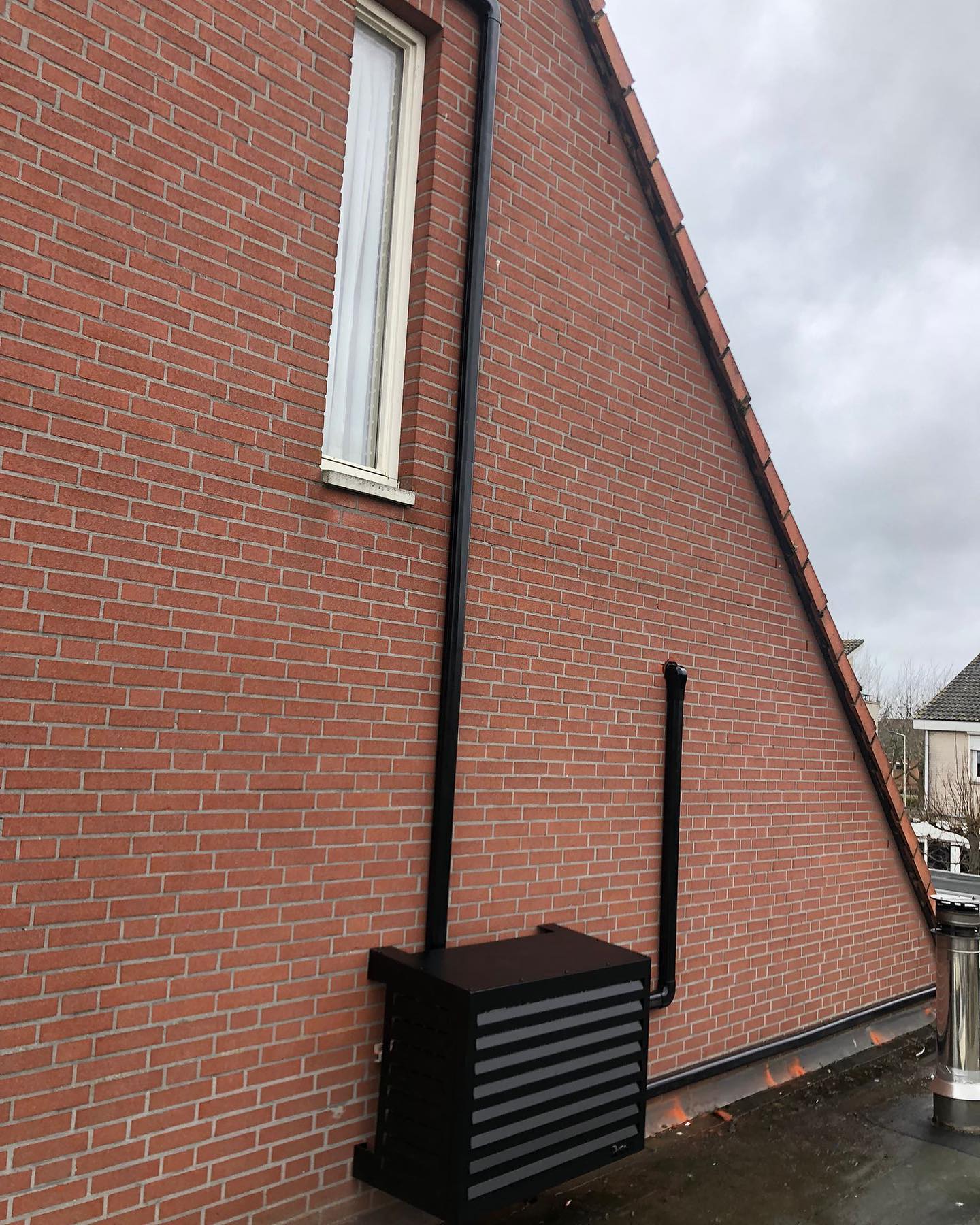 Zwarte ombouw en zwarte leidingen tegen een bakstenen puntgevel
